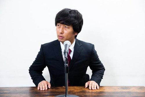 マイクの前で横を向く記者会見中の男性