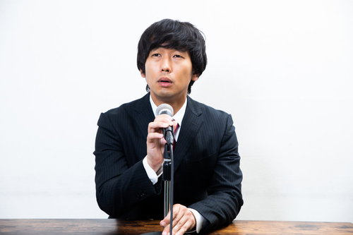 記者会見中にマイク位置を調整する黒いスーツの男性