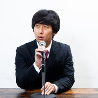 マイク位置を気にしながら真剣に対応する会見する男性の写真