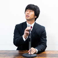 マイクの調子の悪さを目で訴える黒いスーツの男性の写真