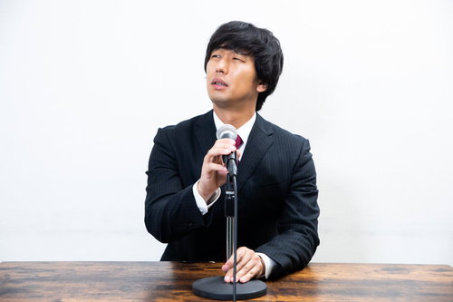 マイクの調子の悪さを目で訴える黒いスーツの男性