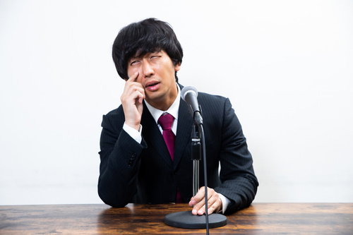 スーツ姿で謝罪する男性の記者会見、手を額に当てて困惑する表情