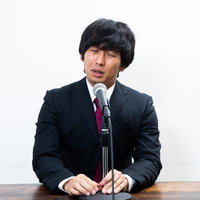 マイクの前で謝罪会見をする黒いスーツの男性の写真