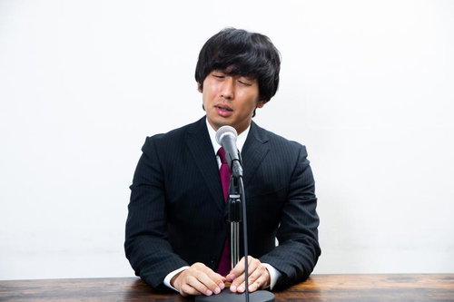 マイクの前で謝罪会見をする黒いスーツの男性