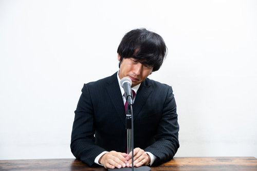 謝罪会見で涙を流し頭を下げる黒いスーツ姿の男性