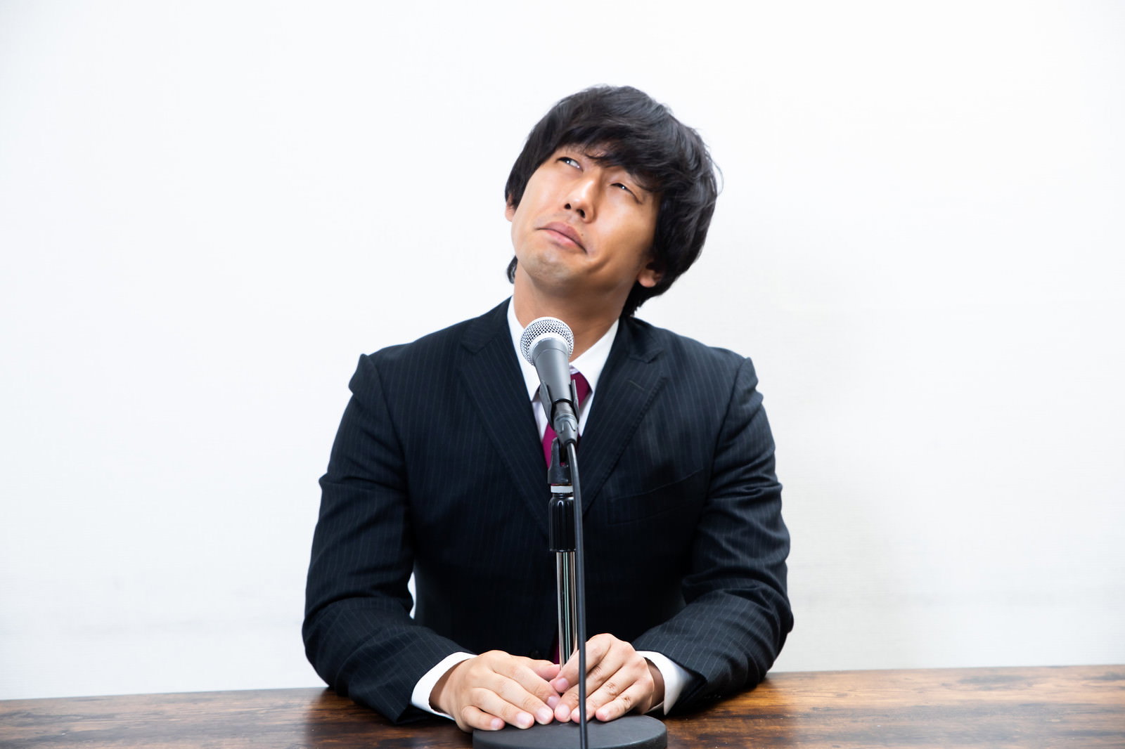 黒いスーツを着た男性が謝罪会見でマイクの前に座っている［モデル：大川竜弥］