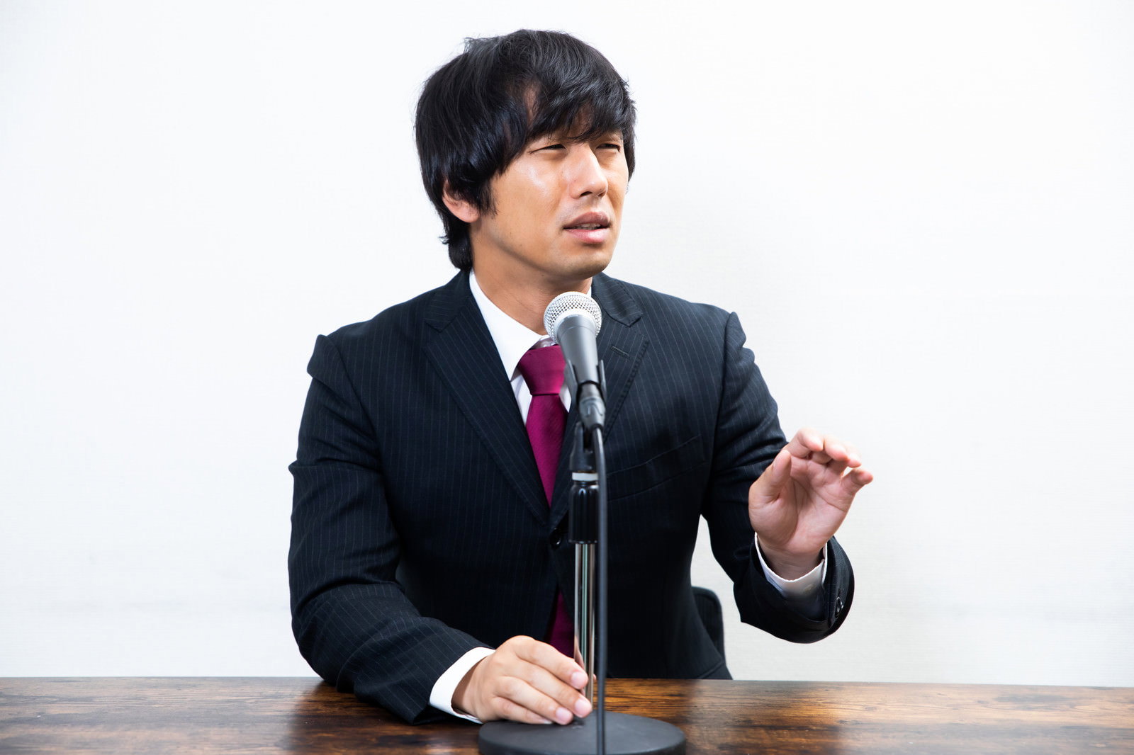 記者会見で困惑した表情を見せるスーツ姿の男性［モデル：大川竜弥］