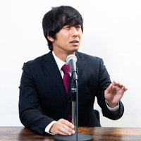 記者会見で言い返せない男性、厳しい質問に戸惑う表情の写真