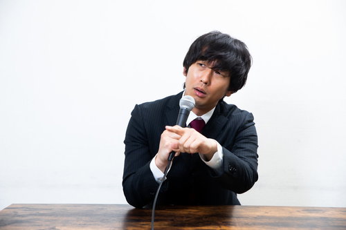 会見中に質問した記者を煽る黒いスーツ姿の男性