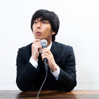 的確な質問に頷くスーツ姿の広報担当男性による記者会見対応の写真