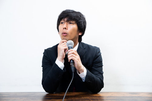 的確な質問に頷くスーツ姿の広報担当男性による記者会見対応