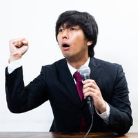 マイクを使って力説する男性のビジネススピーチシーンの写真