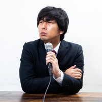 批判をうけてムッとする男性役員がマイクで演説の写真