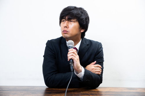 批判をうけてムッとする男性役員がマイクで演説