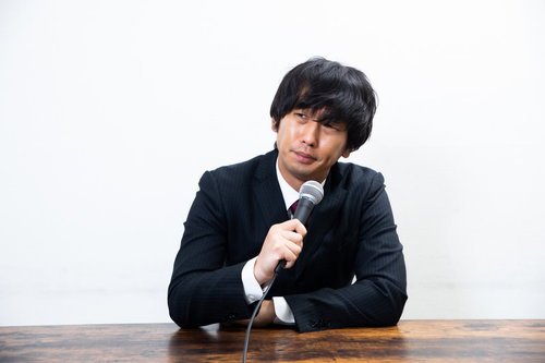記者会見で無愛想にマイクを持つ男性