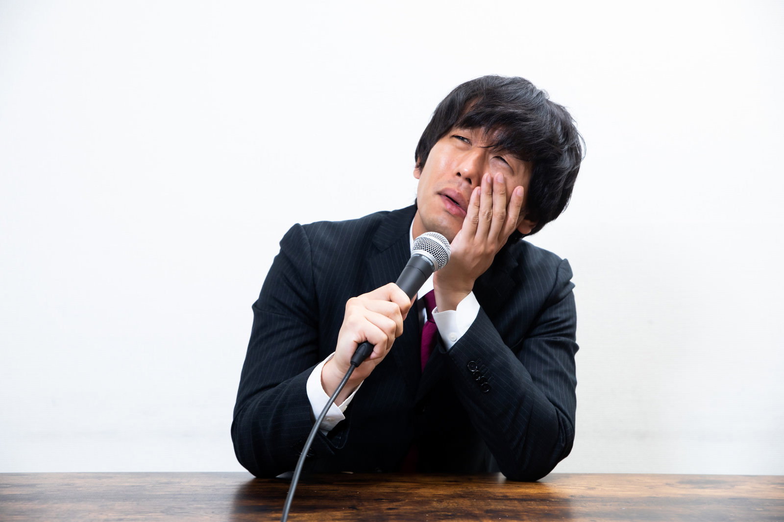 記者会見で涙を流しながら手を顔に当てる黒いスーツの男性［モデル：大川竜弥］