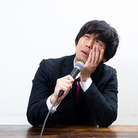 記者会見中に涙して悔しさを語る黒いスーツの男性の写真