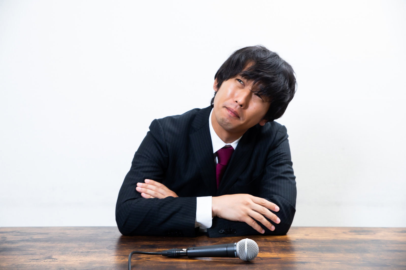 黒いスーツを着て困った表情で腕を組み考え込む男性