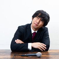 マイクの前で困った表情で考え込む男性社員の写真