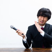 嫌がりながらマイクを向ける男性の記者会見での発言場面の写真