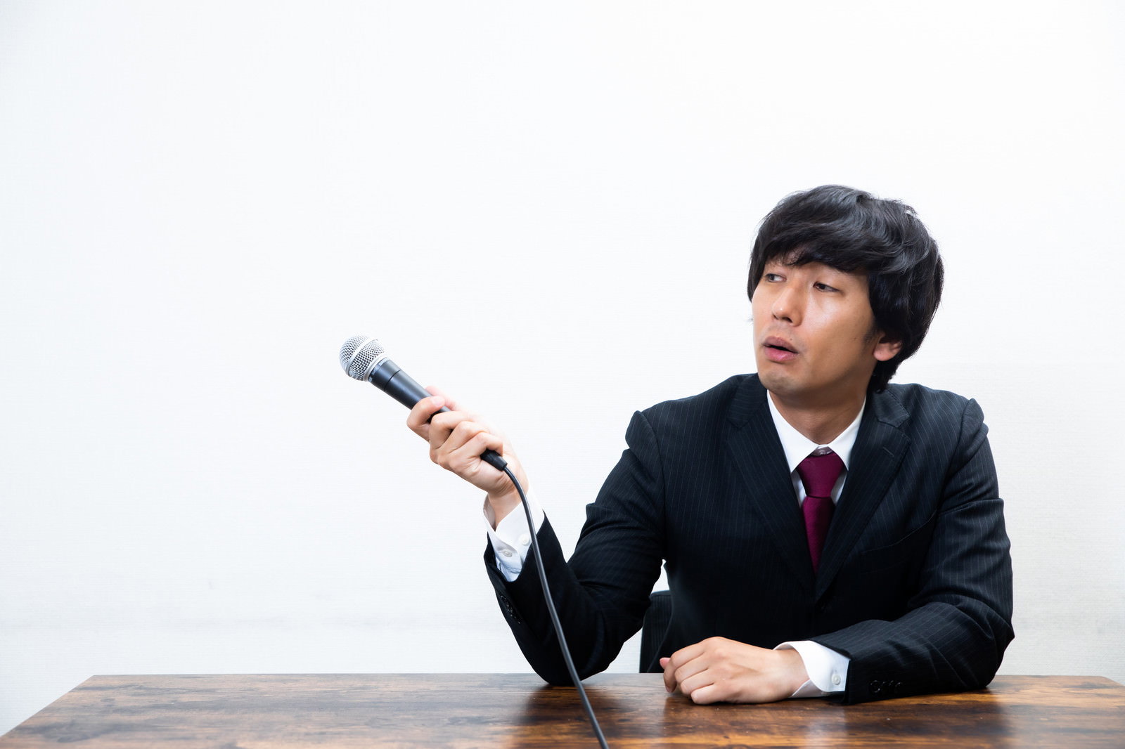 机に座りマイクを持って横を向く男性［モデル：大川竜弥］