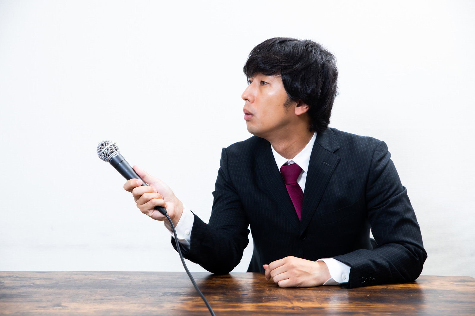 黒いスーツを着た男性がマイクを向けてコメントを求めている［モデル：大川竜弥］