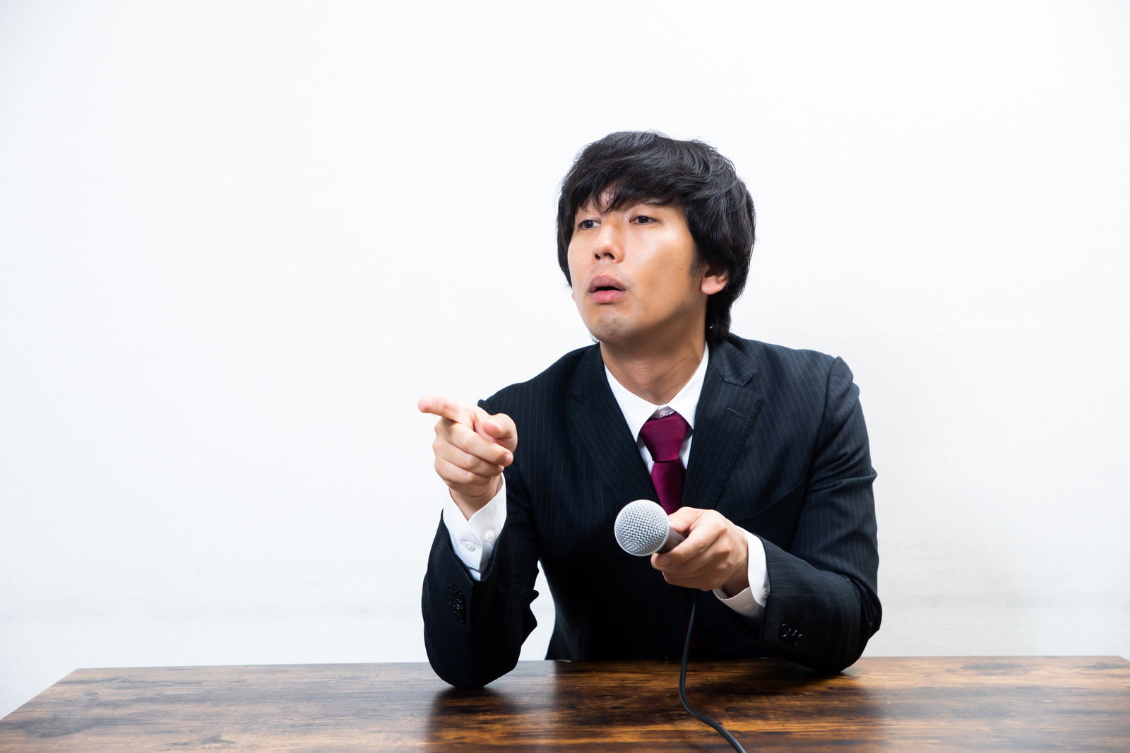 黒いスーツを着た男性が机に座り指をさして怒っている様子［モデル：大川竜弥］
