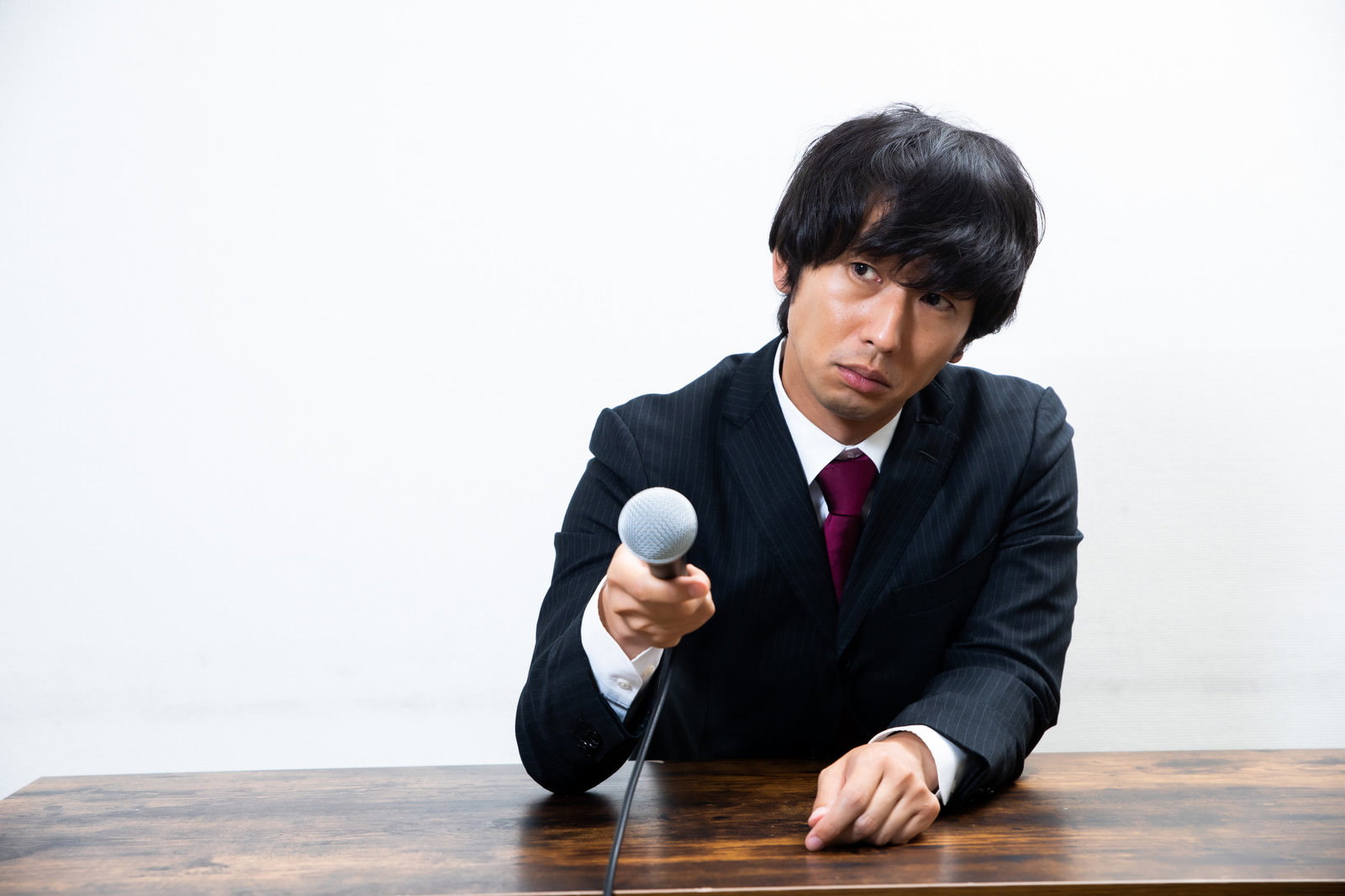 黒いスーツを着た男性がマイクを向けられて困った表情をしている［モデル：大川竜弥］