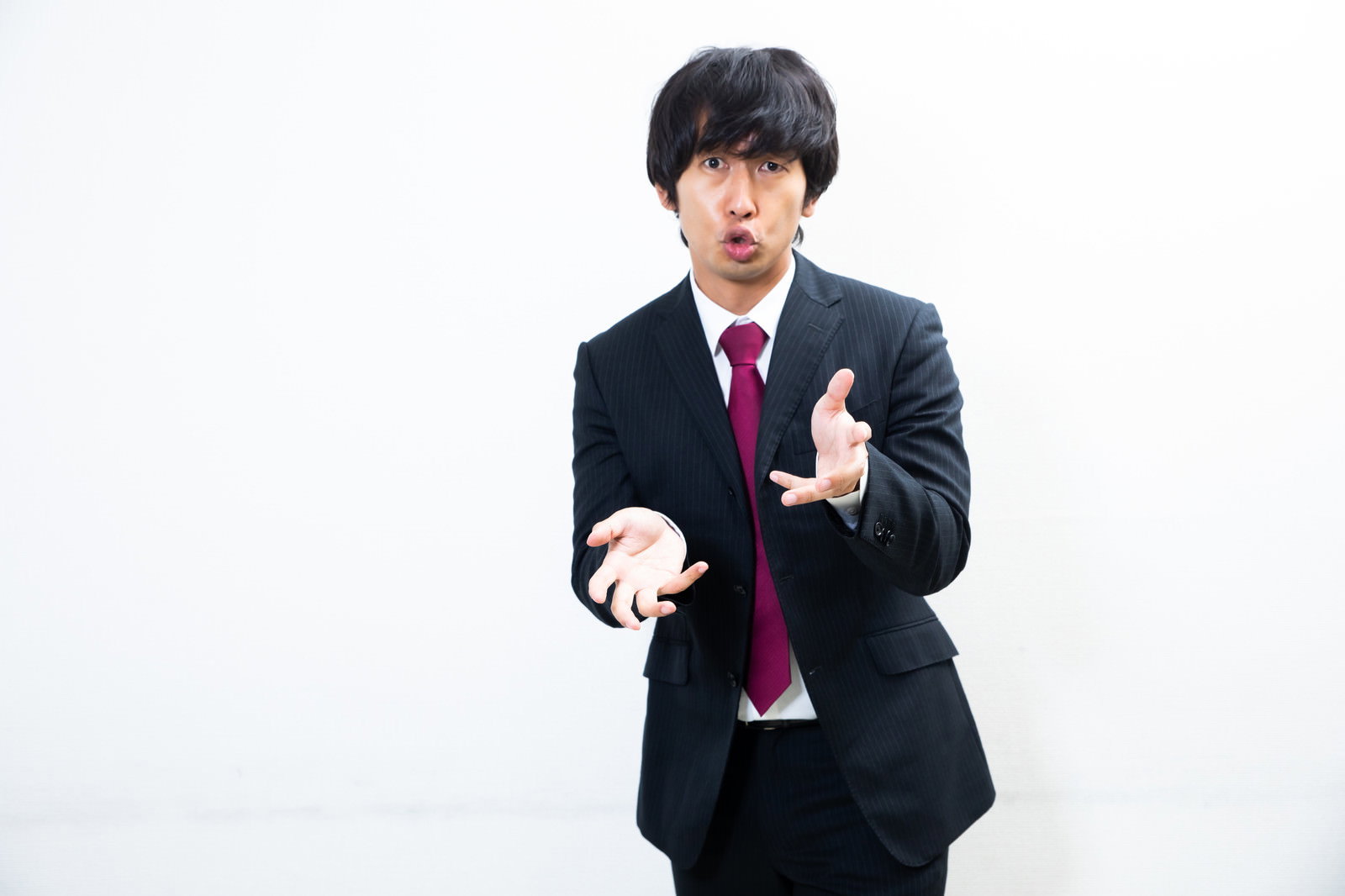 黒いスーツを着た男性が両手を広げて感情的に説明している［モデル：大川竜弥］
