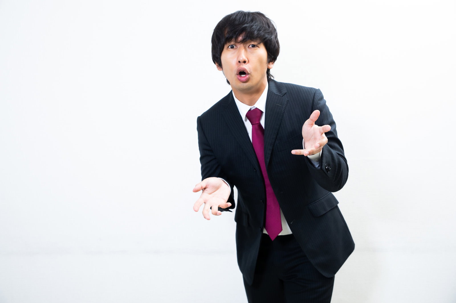 黒いスーツに赤いネクタイの会社員が片手を前に突き出して力説している［モデル：大川竜弥］