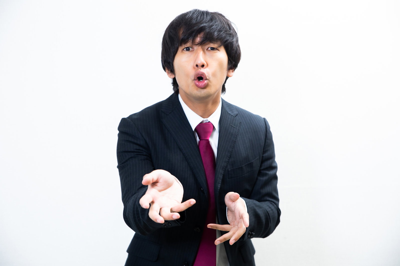黒いスーツに赤いネクタイを着た男性が前のめりになって力説している様子［モデル：大川竜弥］