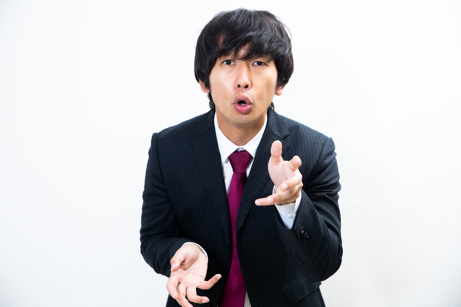 黒いスーツを着た男性が右手の人差し指を立てて説明している［モデル：大川竜弥］