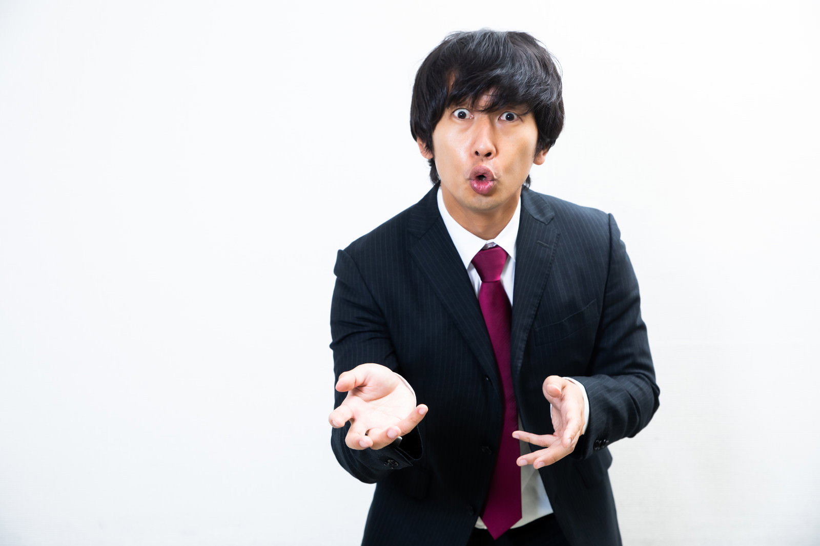 黒いスーツに赤いネクタイを着た男性が両手を使って力説している［モデル：大川竜弥］