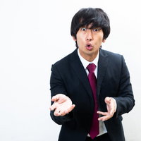 両手を使って力説する登壇男性のビジネス会見の写真