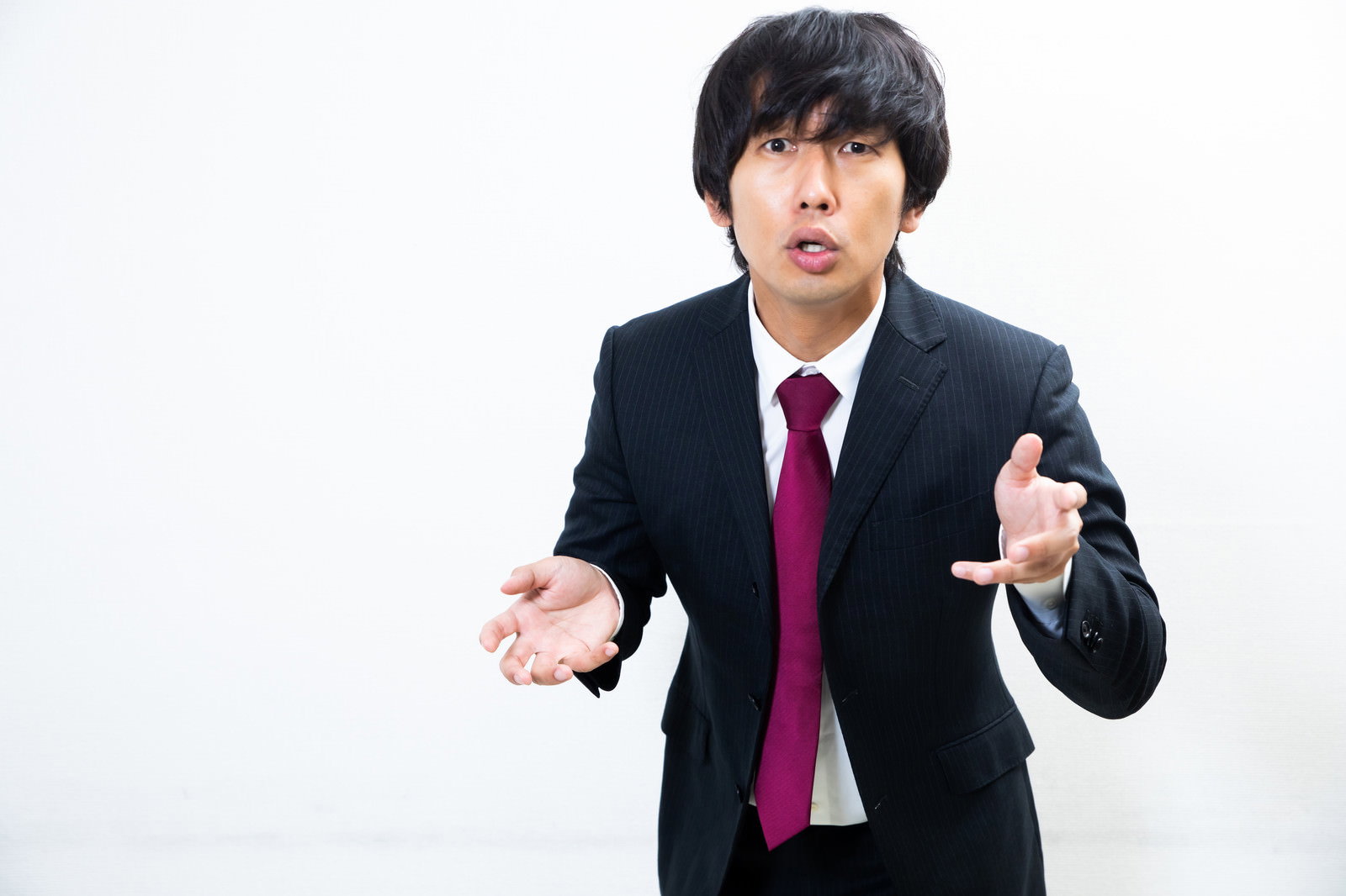 黒いスーツを着た男性が両手を広げて驚いた表情を見せている［モデル：大川竜弥］