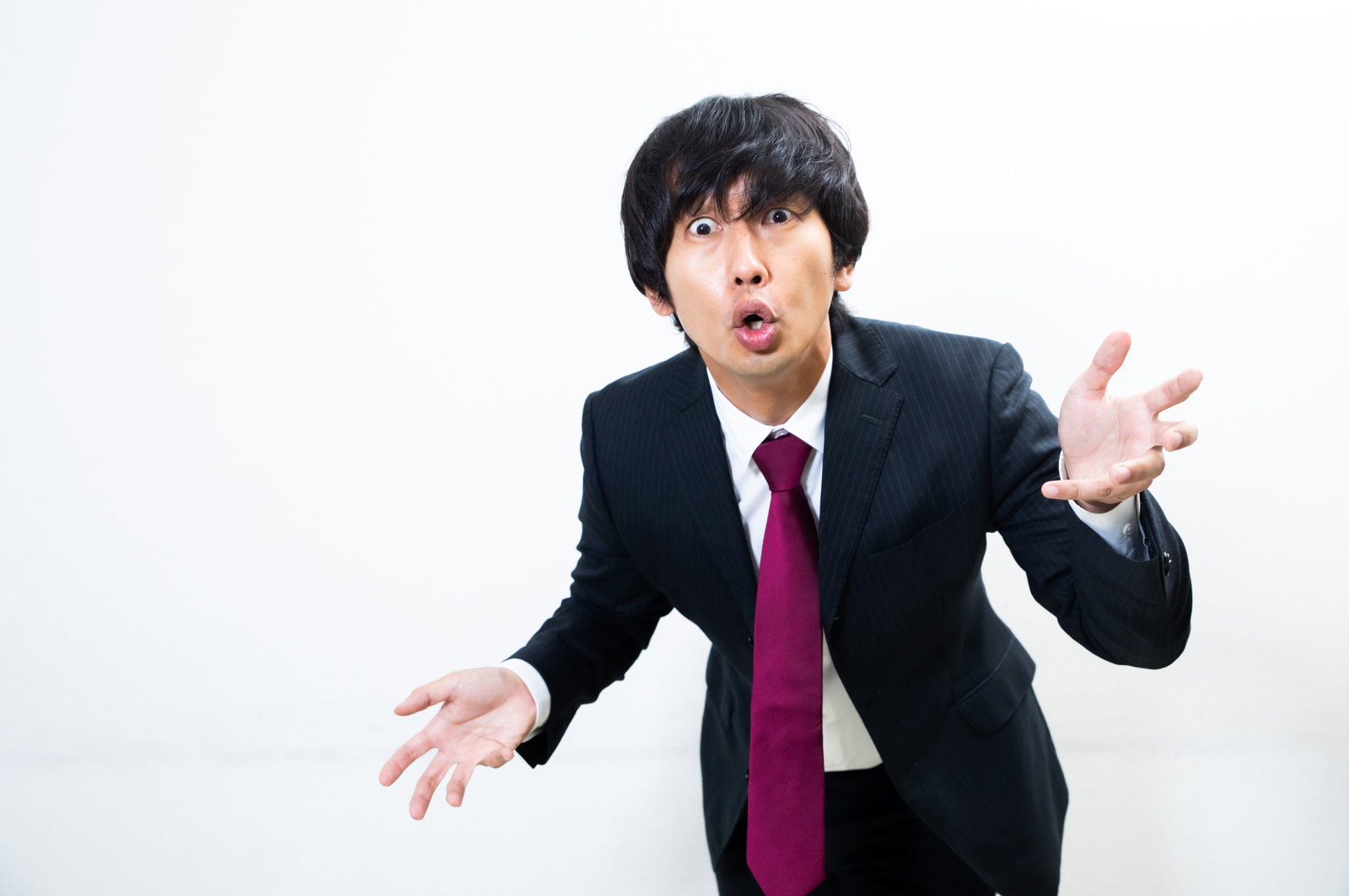 紺色のスーツに赤いネクタイの男性が両手を広げて熱弁を振るっている様子［モデル：大川竜弥］