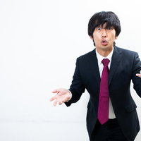 手振り意識しすぎでしょ、両手を広げて説明するスーツ姿の男性の写真