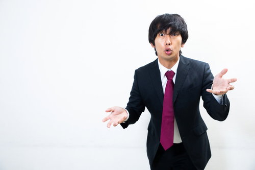 手振り意識しすぎでしょ、両手を広げて説明するスーツ姿の男性