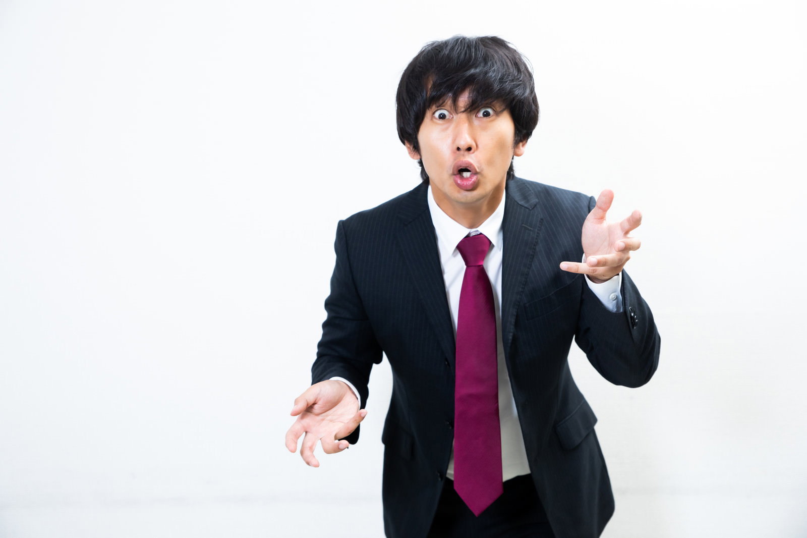 黒いスーツに赤いネクタイの男性が両手を広げて熱弁している［モデル：大川竜弥］