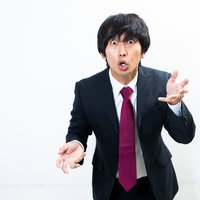 両手を広げて力説する黒スーツの男性の演説風景の写真