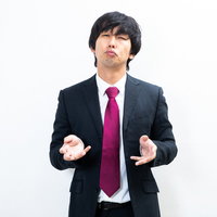 やる気のない会見で両手を広げるスーツ姿の男性の写真