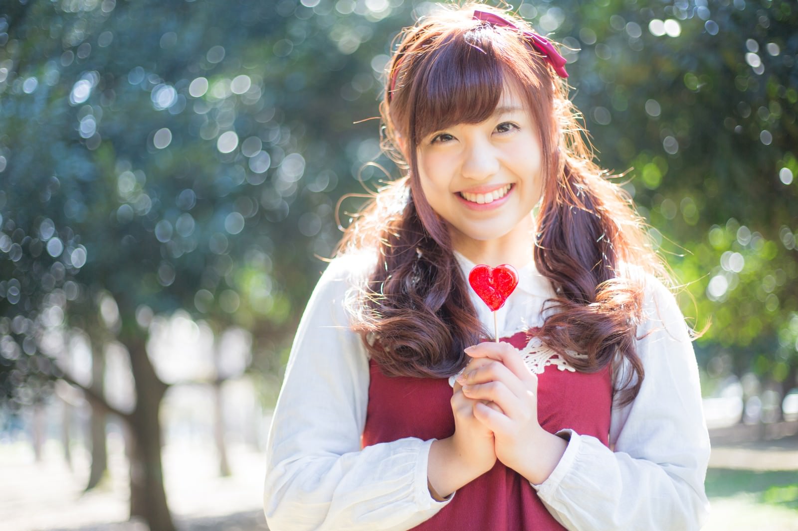 赤いハート型のキャンディを持って笑顔の森ガール女性［モデル：河村友歌］