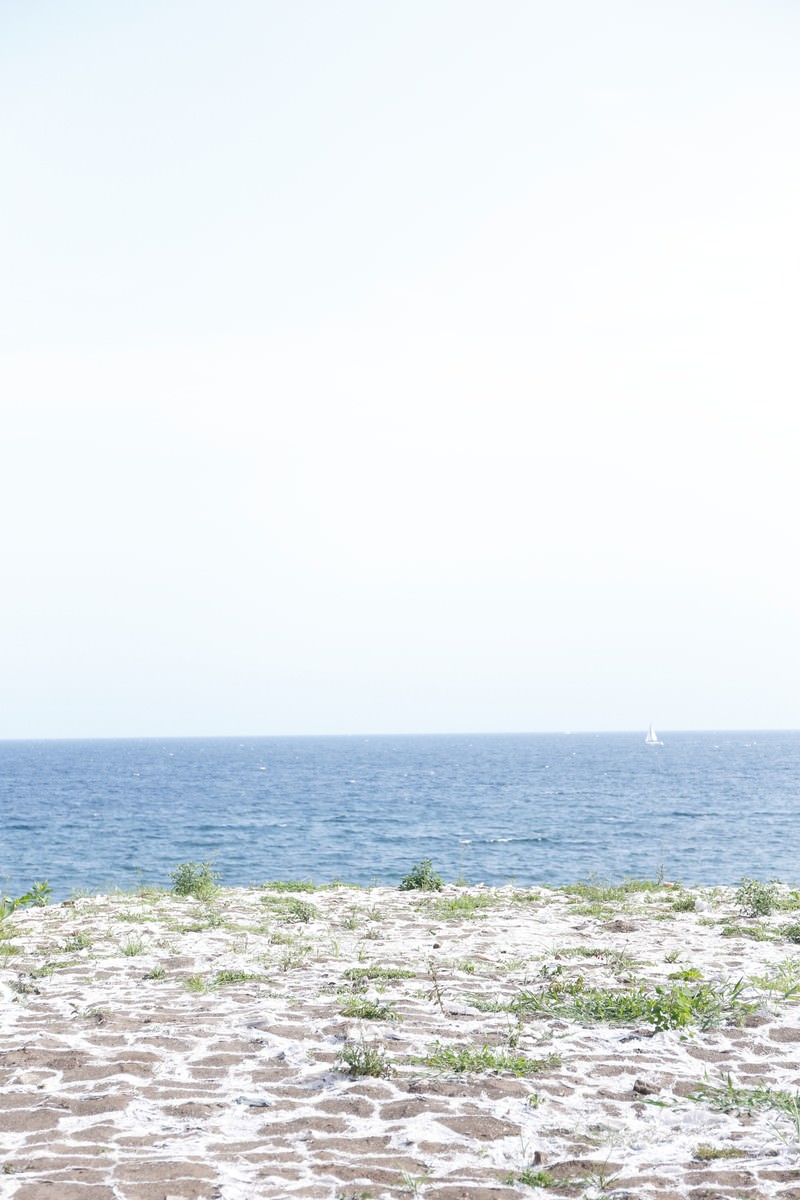 草が生える砂浜から見た青い海とセーリングボート