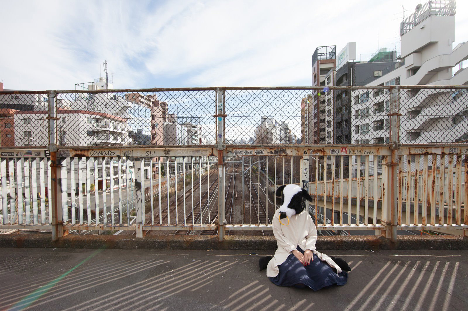 エト牛のかぶり物をした女性が都市の高架下で座り込んでいる［モデル：古性のっち］