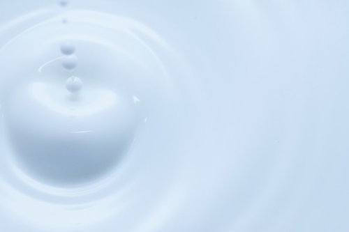 淡い明るい背景で水面に波紋を広げる空中の水滴の接写