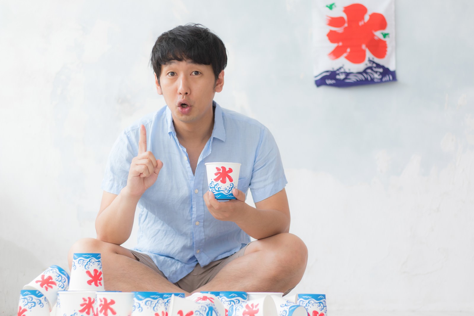 赤と青の花柄かき氷を持ち、指を立てながら口を開ける男性［モデル：大川竜弥］