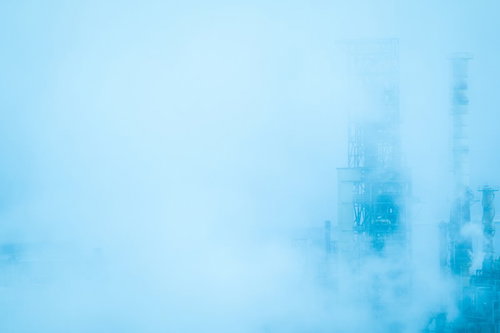 靄に包まれた工場施設、煙突とクレーンが立ち並ぶ濃霧の産業地帯