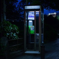 夜間に照らされた怪談めいた公衆電話ボックスと街灯の写真