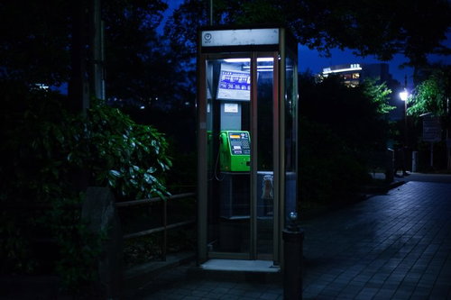 夜間に照らされた怪談めいた公衆電話ボックスと街灯