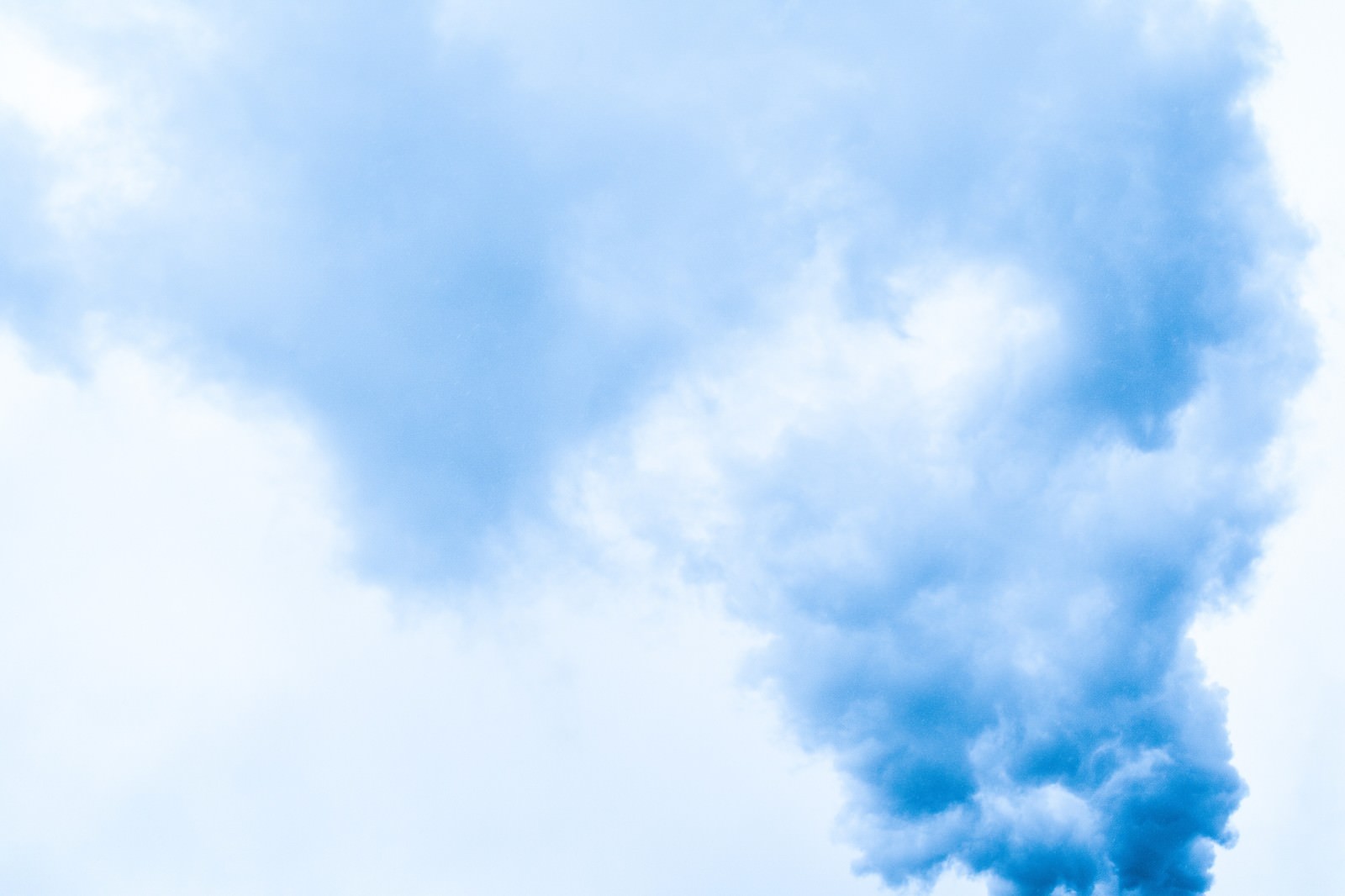 青空に白い煙が風に流されて渦を巻きながら上昇している